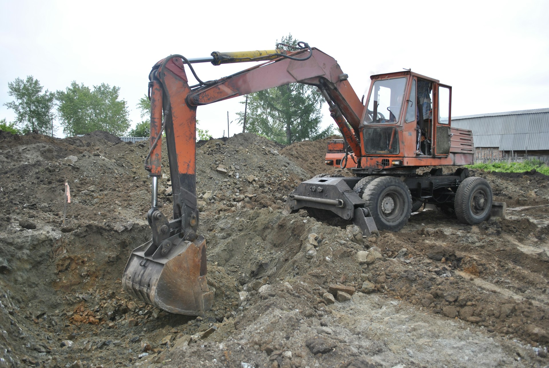 An image of an excavator doing excavation services in the dirt in front of a house.